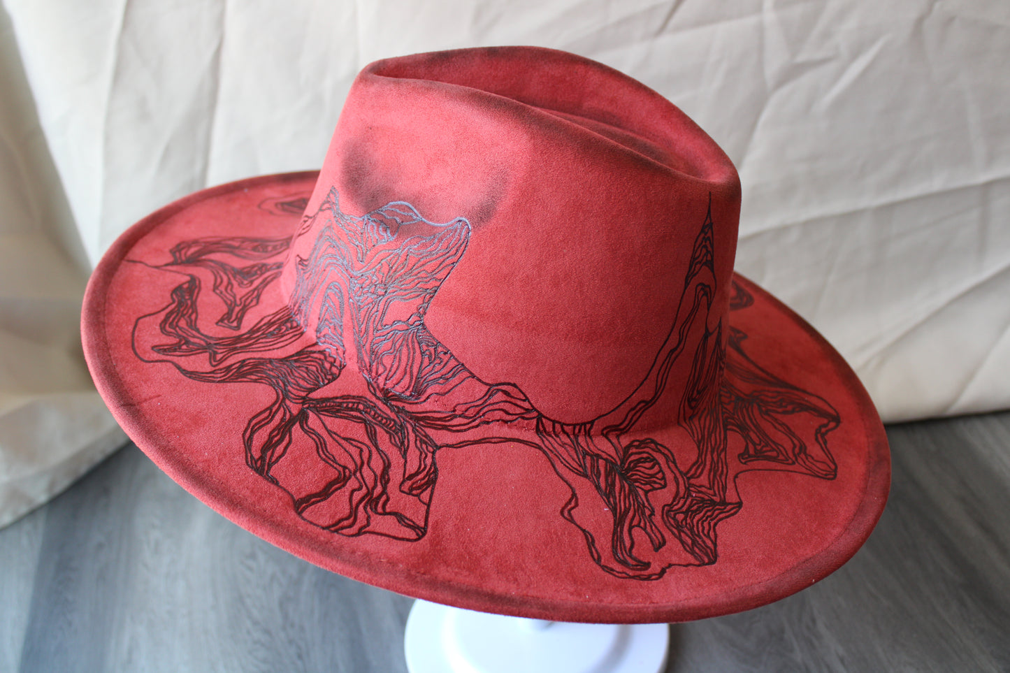 a red-orange wide brim feodra with a topographical design burned in
