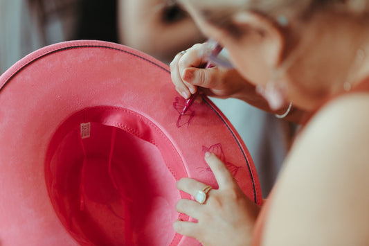 a woman draws on the underside of a pink fedora