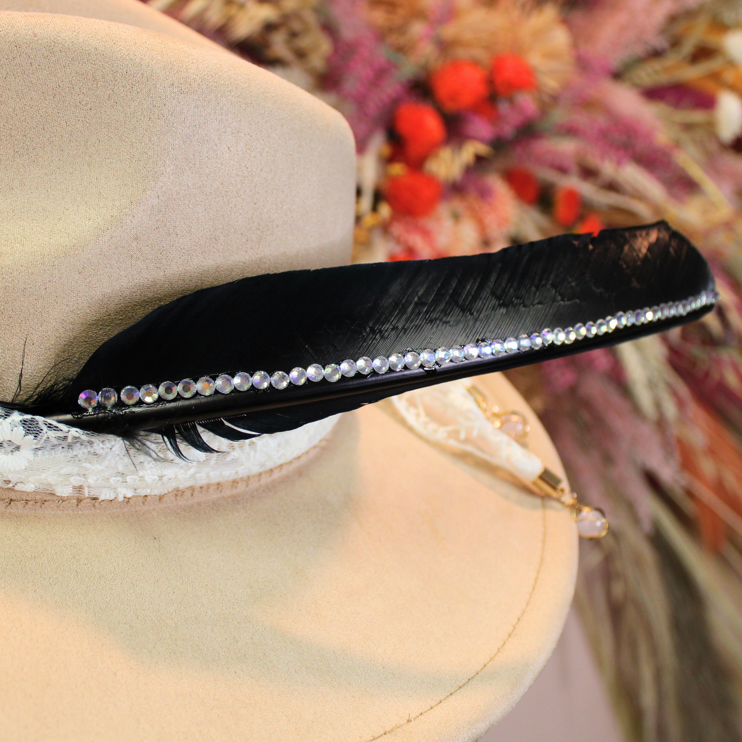 a black turkey pointer feather embellished with rhinestones shown on a beige fedora