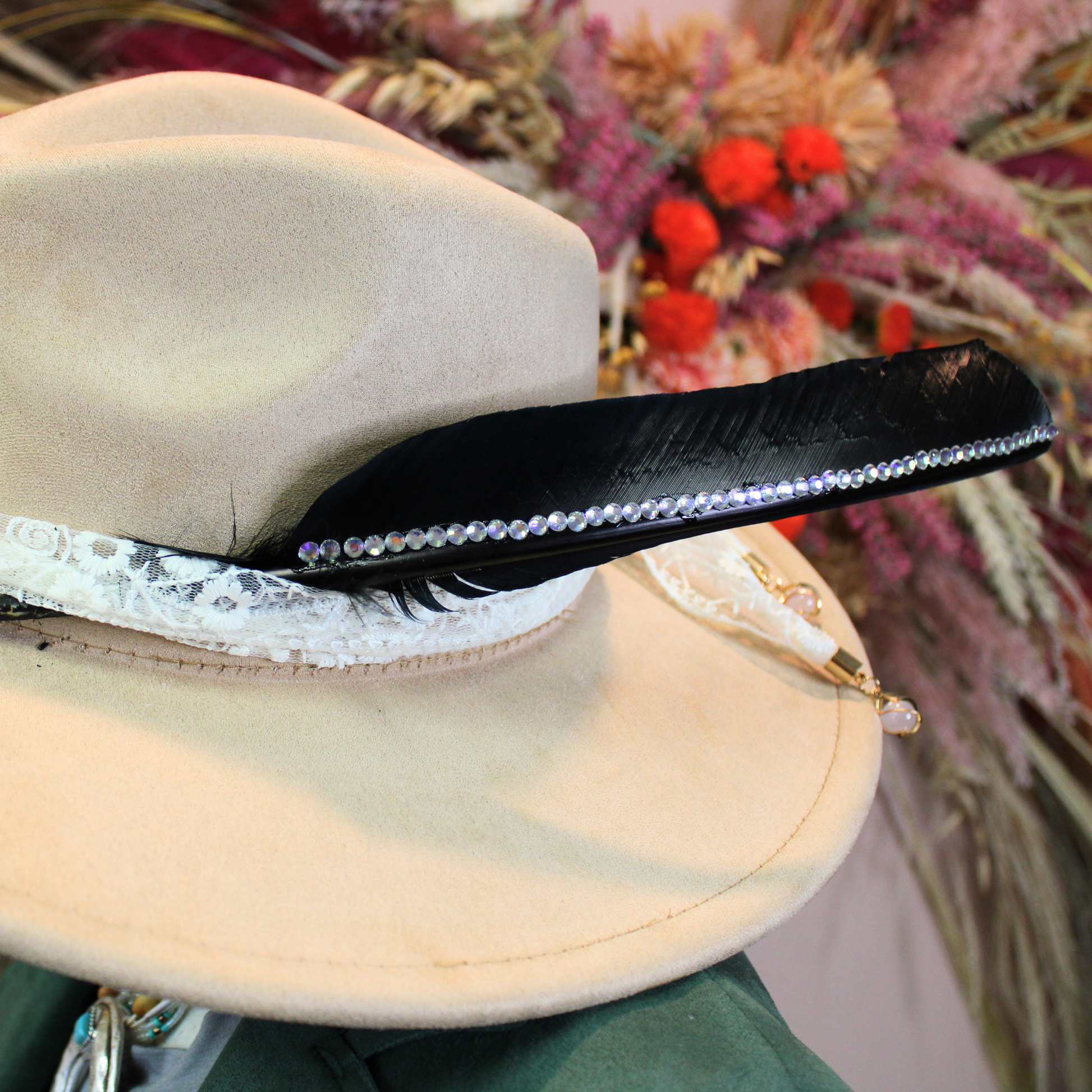 a black turkey pointer feather embellished with rhinestones shown on a beige fedora